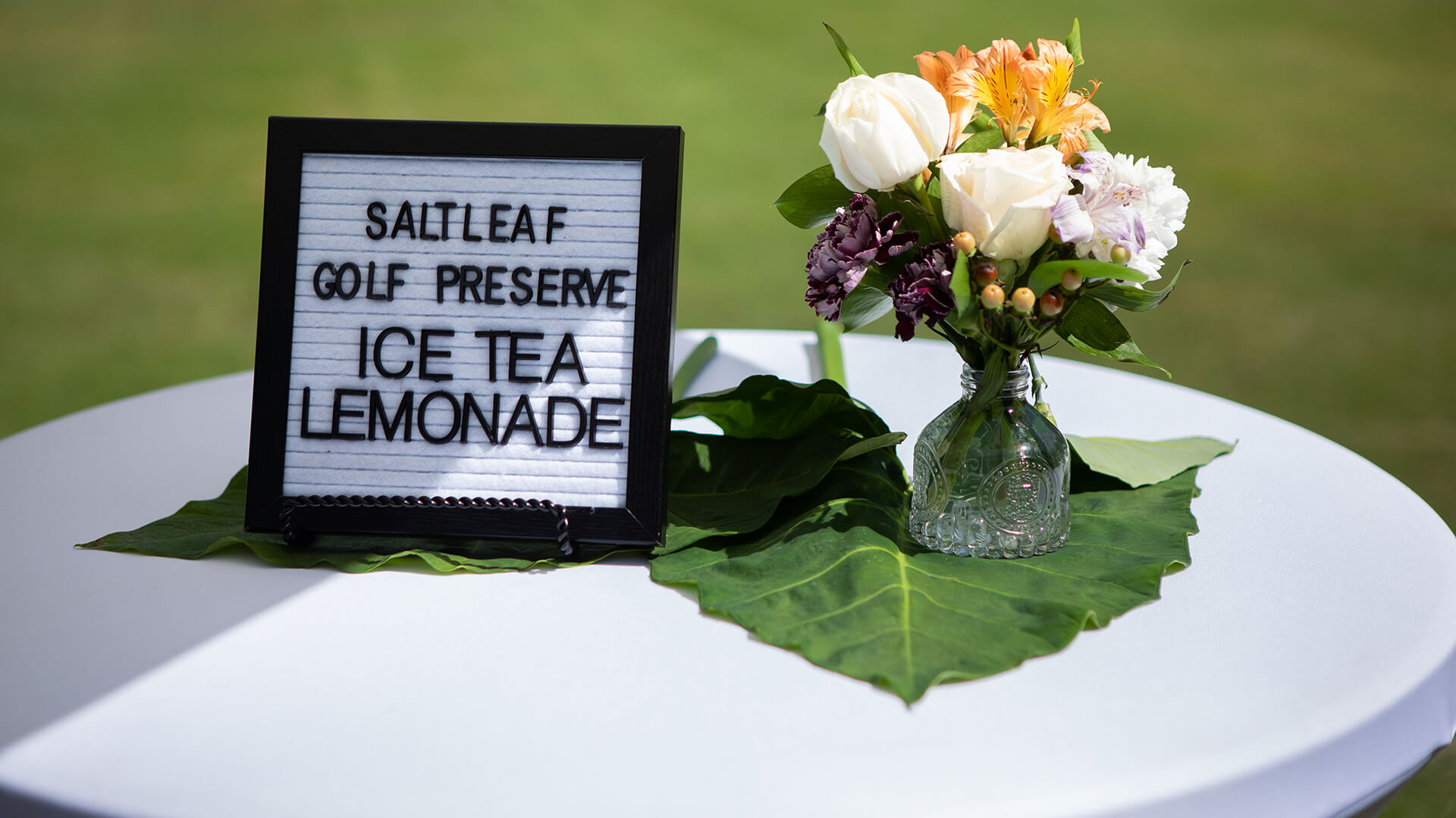 A table adorned with beautiful flowers and a sign that says "ice tea lemonade" at the Saltleaf Golf Preserve in Bonita Springs, offering a refreshing break after playing a round at this