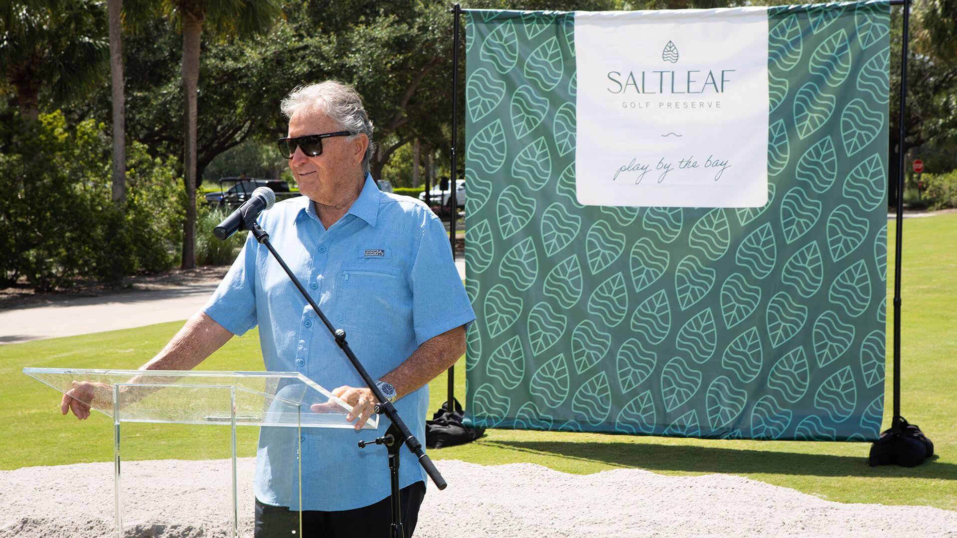 A man standing at a podium in front of a Saltleaf Golf Preserve green screen.