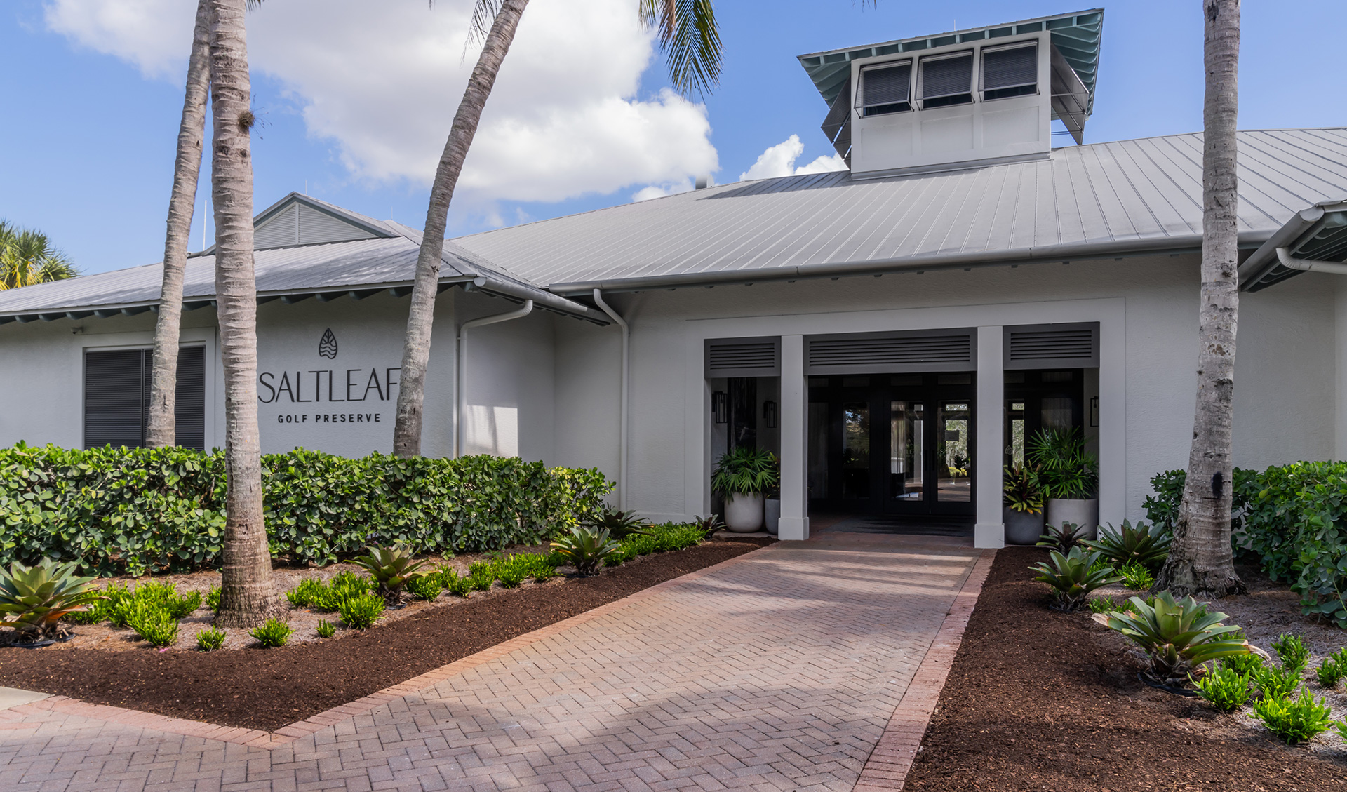 The entrance to the Saltleaf Golf Preserve building in Bonita Springs, with palm trees and bushes.