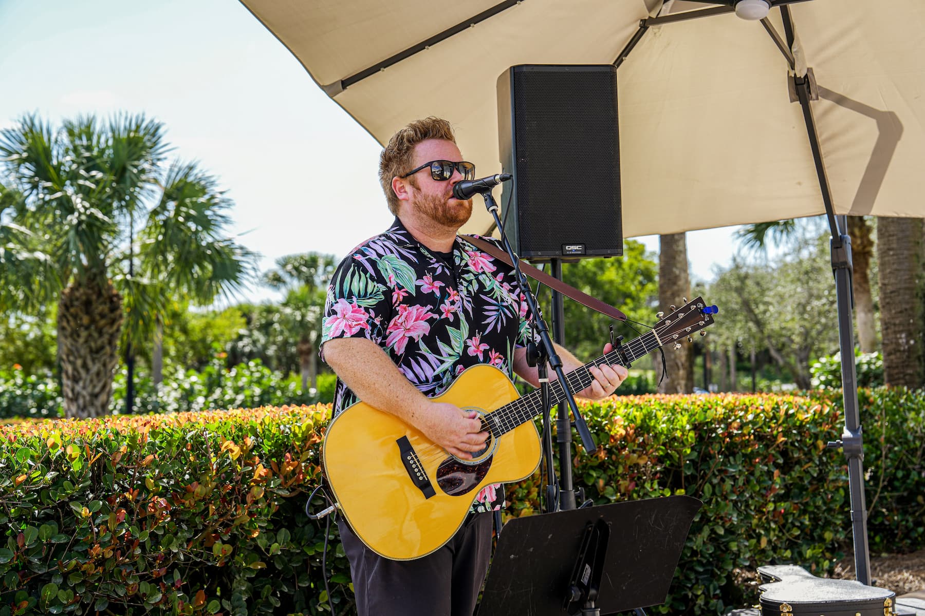 A man in a hawaiian shirt playing an acoustic guitar.