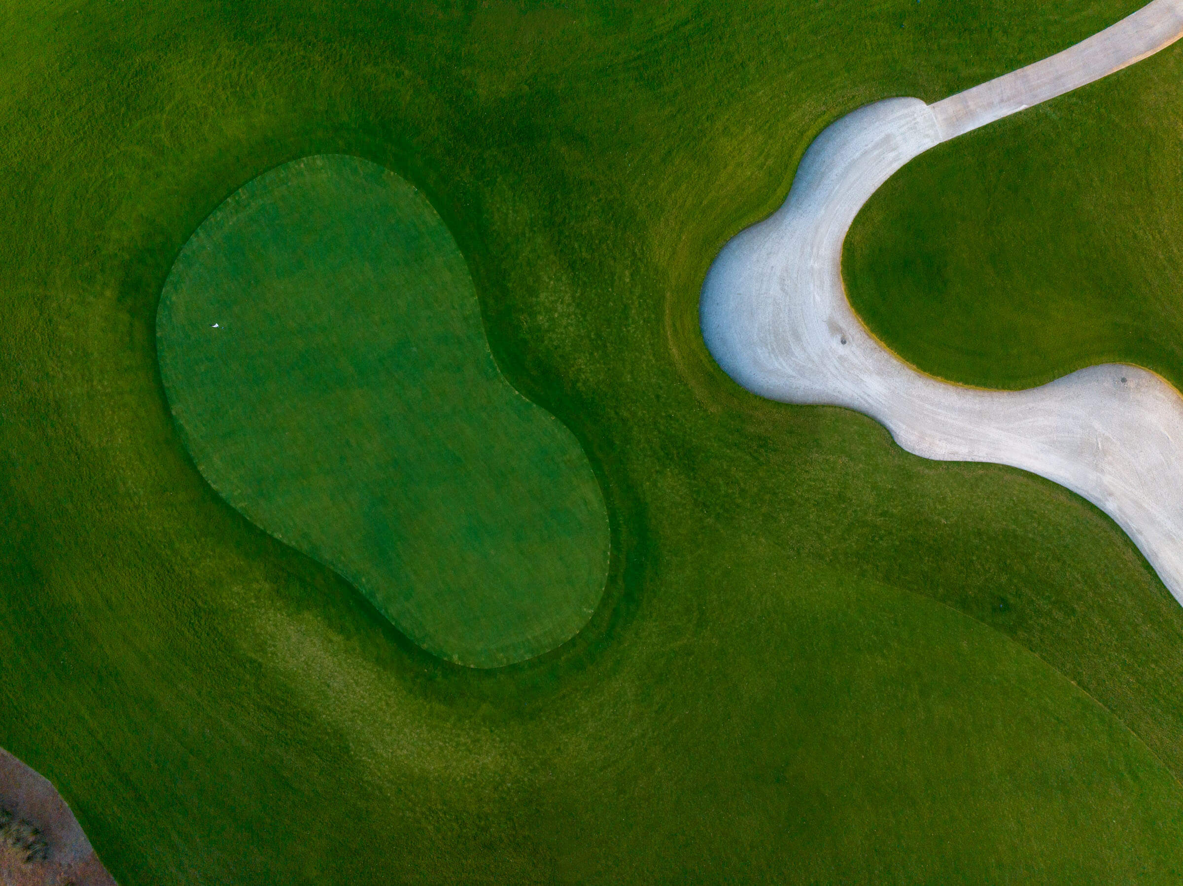 Aerial view of a golf course showing a green and a sand bunker surrounded by a winding path.